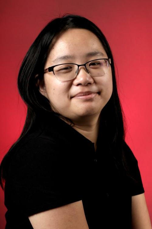 Portrait of Casey Chung in the black Digital Media Studio 1308 shirt against a red backdrop